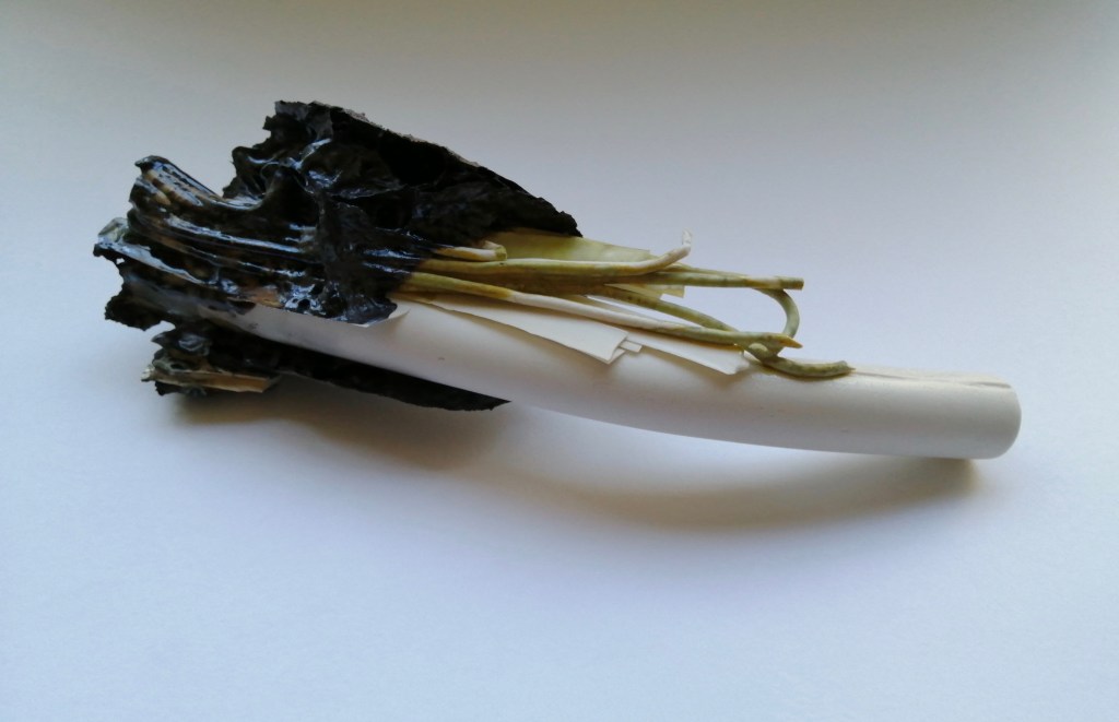 porcelain sculpture with a white pipe and strands of green tinged porcelain emerging from a melted brick and glaze.